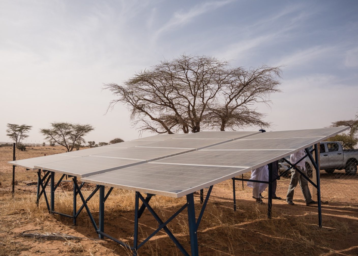 Ground-mounted solar array in the Mauritanian bush with a pickup truck and team in traditional dress